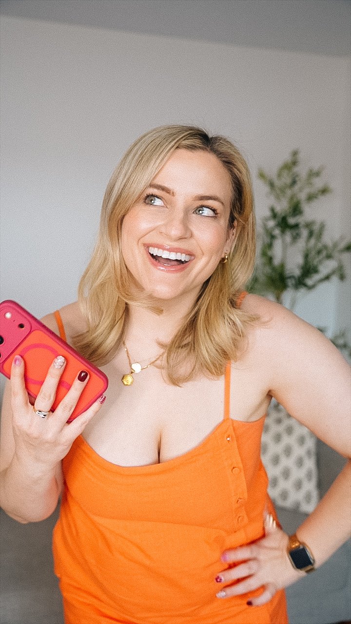 The Patti Q Edit in Orange with iphone and smiling